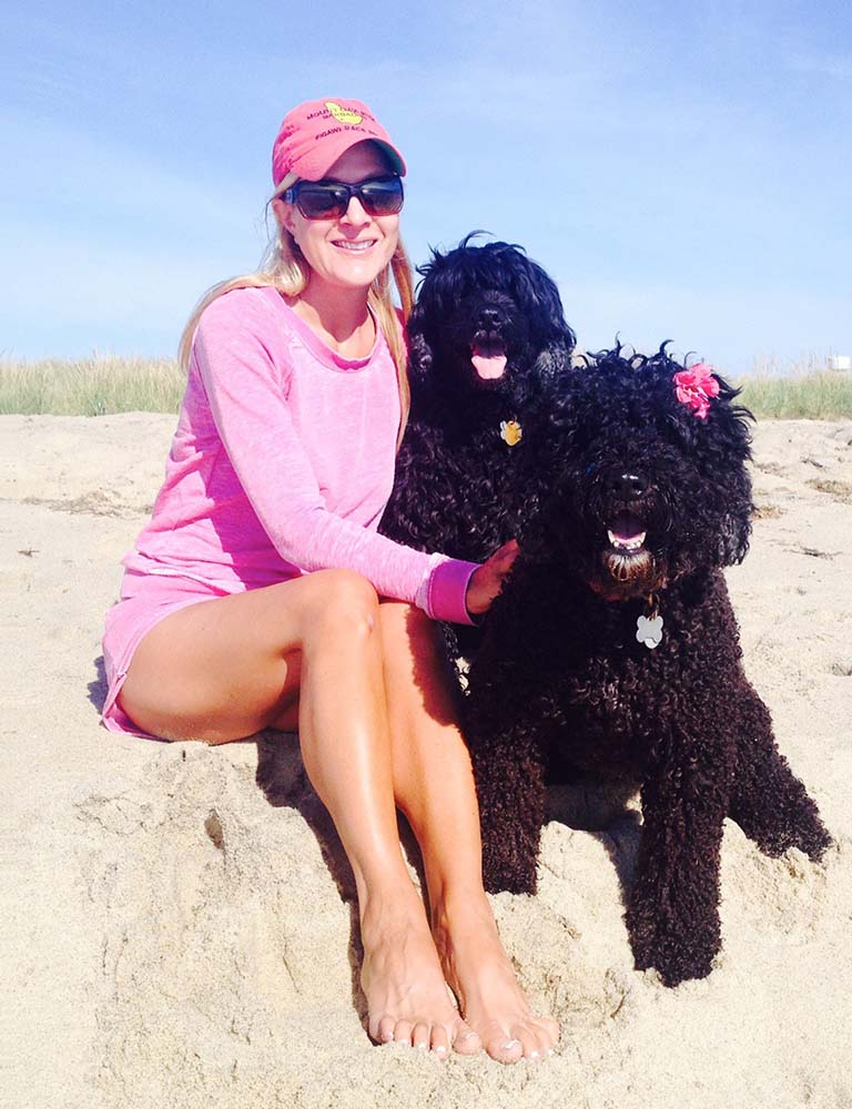 Marci sitting on the beach with her two black dogs